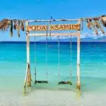 Plage de Ksamil avec des eaux turquoises et une balançoire en bois dans l'eau, suggérant un cadre idyllique pour la plongée à Saranda et Ksamil en Albanie