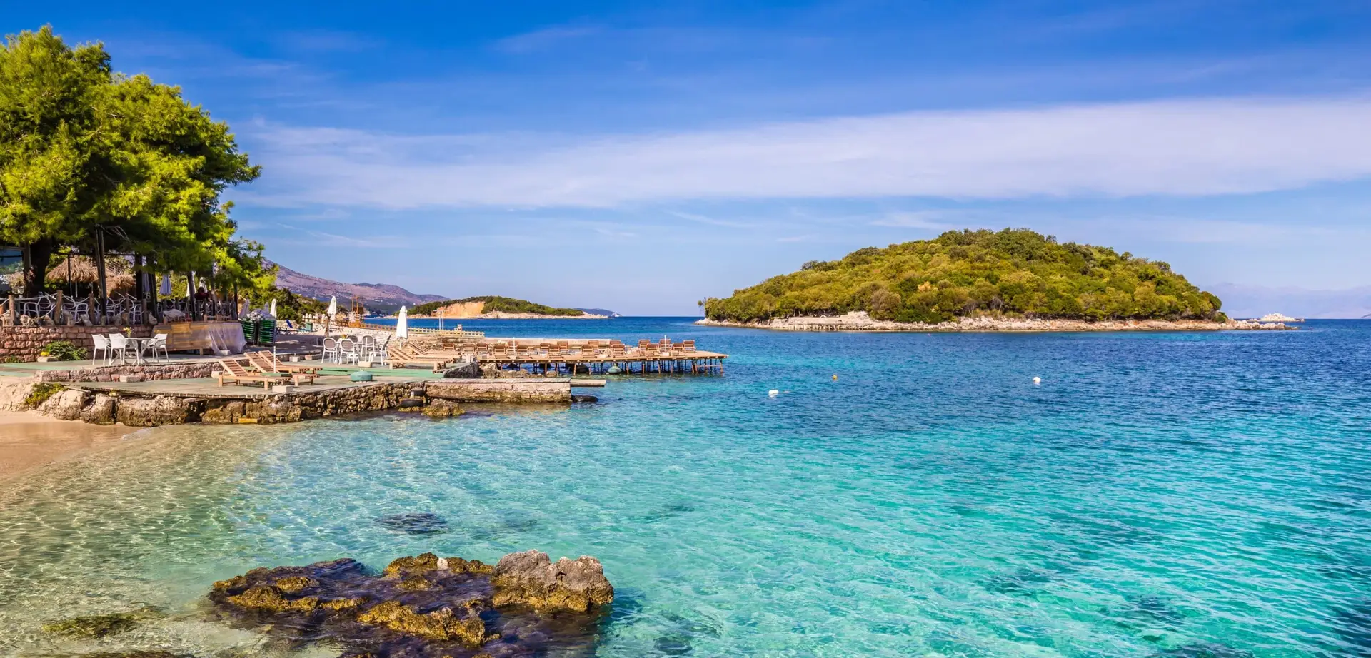 Plage de Vlorë en Albanie avec eau turquoise, pontons en bois et îlot boisé en arrière-plan
