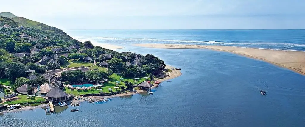 Vue aérienne de l’embouchure de la rivière Umzimvubu à Port St Johns, avec des lodges traditionnels, une plage sauvage et l’océan Indien à l’horizon