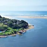 Vue aérienne de l’embouchure de la rivière Umzimvubu à Port St Johns, avec des lodges traditionnels, une plage sauvage et l’océan Indien à l’horizon