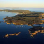 Vue aérienne de l'île de Porquerolles entourée d'eaux bleues et de bateaux au mouillage, un site prisé pour la plongée sous-marine en Méditerranée.