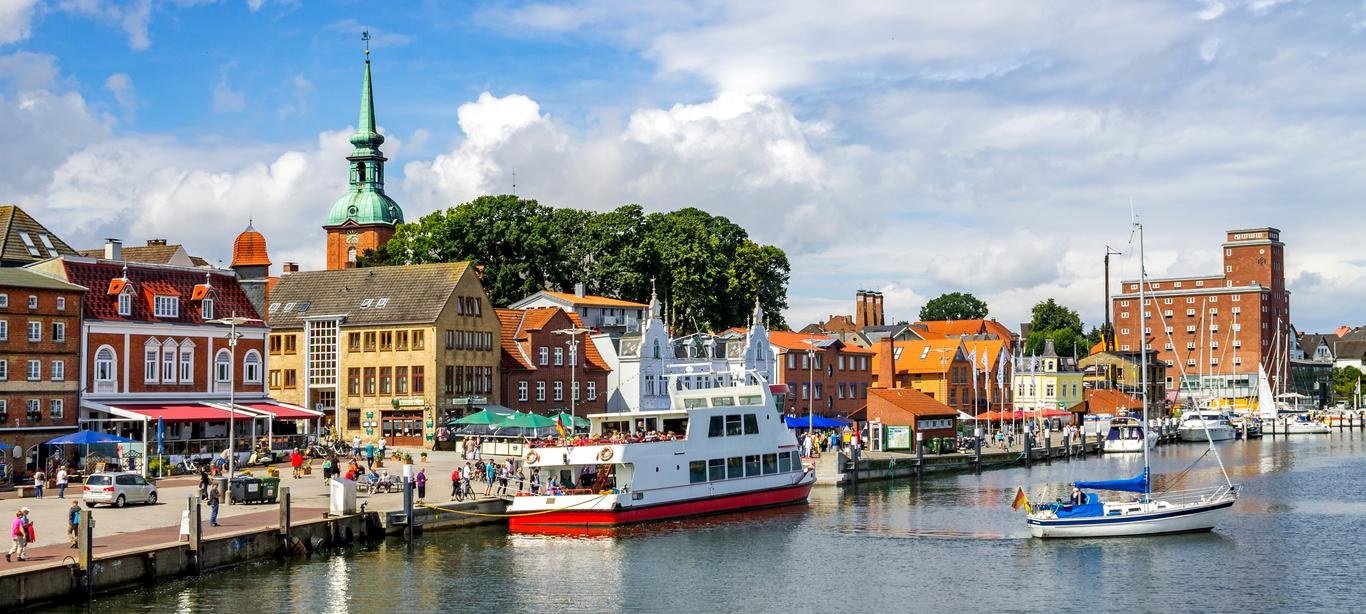 Vue du port de Flensburg avec bateaux, bâtiments colorés et église en arrière-plan, un lieu paisible pour la plongée en mer Baltique