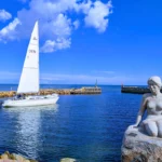 Voilier entrant dans le port d Asaa au Danemark avec une statue en pierre au premier plan et la mer du Kattegat en arrière plan