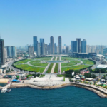 Vue aérienne de Xinghai Square à Dalian avec le front de mer, les gratte-ciel modernes et le parc circulaire en bord de mer.