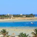 Lagon turquoise à Marsa Alam en mer Rouge avec récif corallien, plage bordée de palmiers et bateau de plongée au large